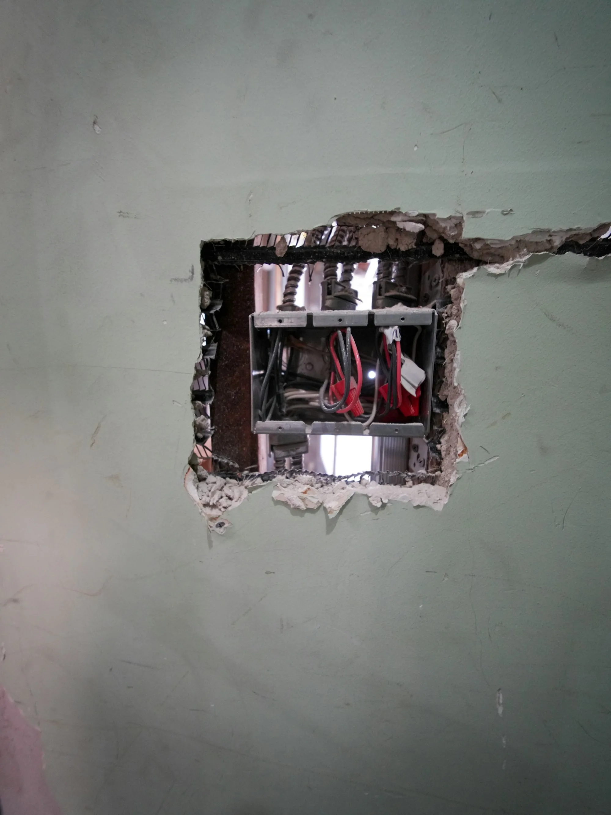 Hole cut into a wall exposing wiring and pipes